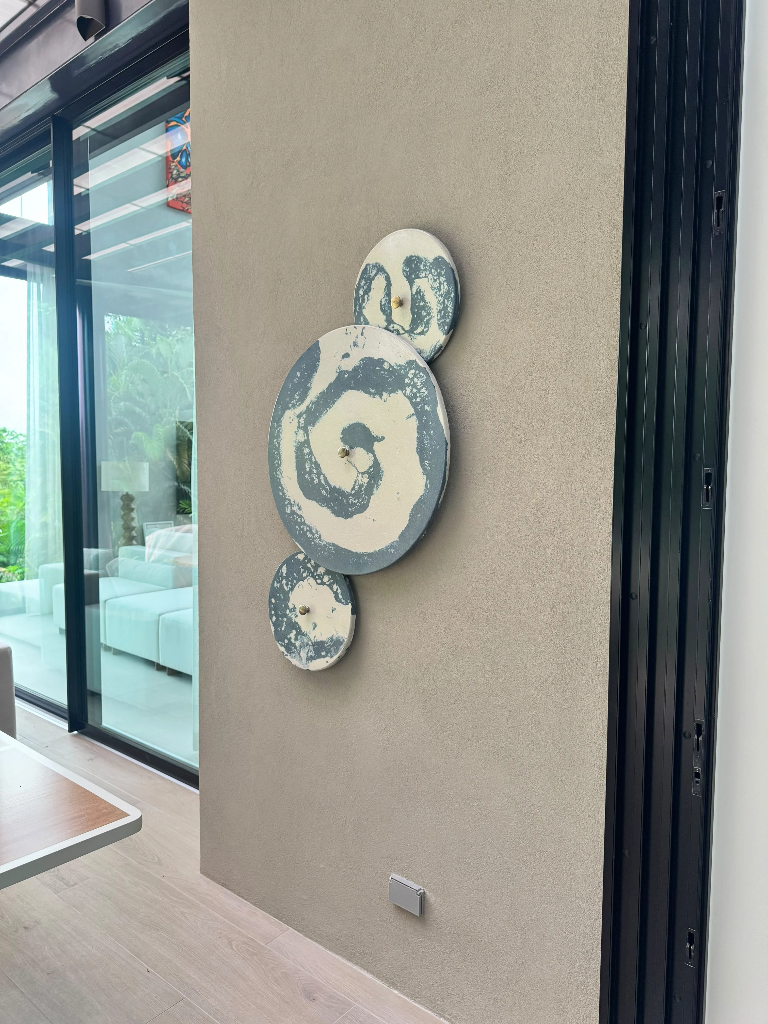 Tres discos decorativos de concreto con remolinos blancos y azulados, fijados a una pared lisa junto a un ventanal