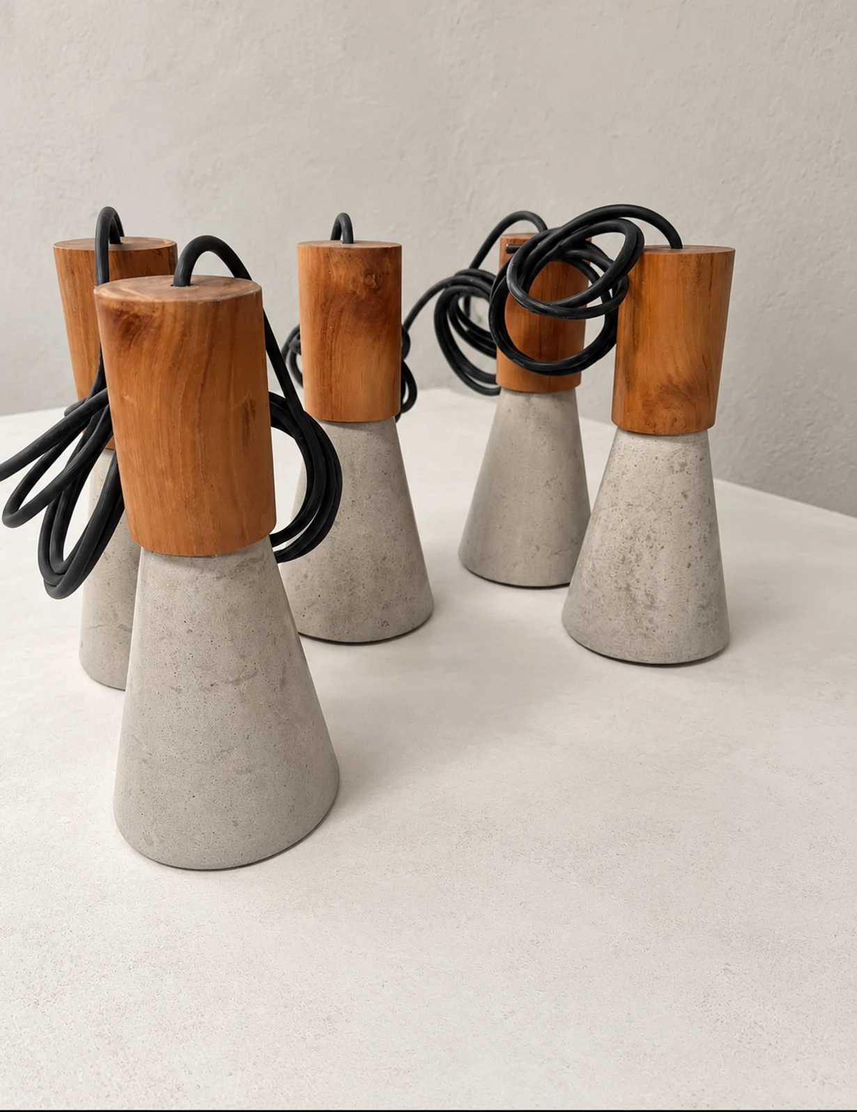 Lámparas colgantes con base cónica de concreto gris, cuerpo cilíndrico de madera y cable negro enrollado, sobre superficie clara
