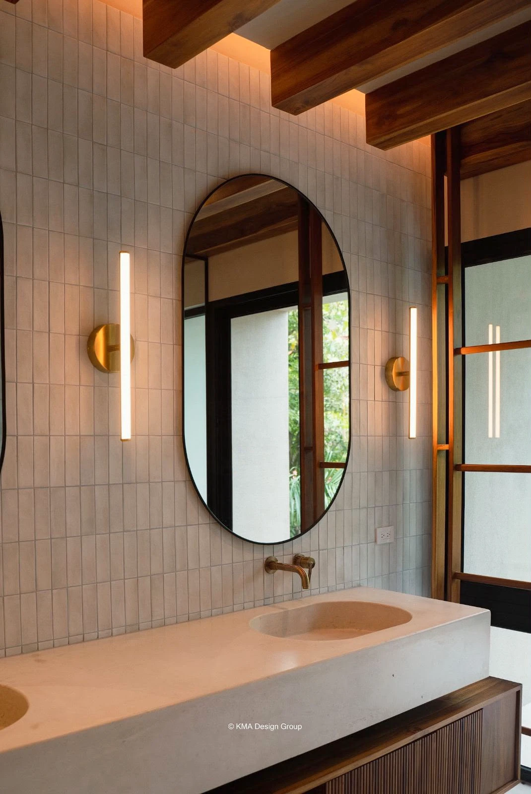 Lavatorio integrado de concreto claro con encimera larga, espejo ovalado, apliques de luz y grifería dorada en baño con azulejos