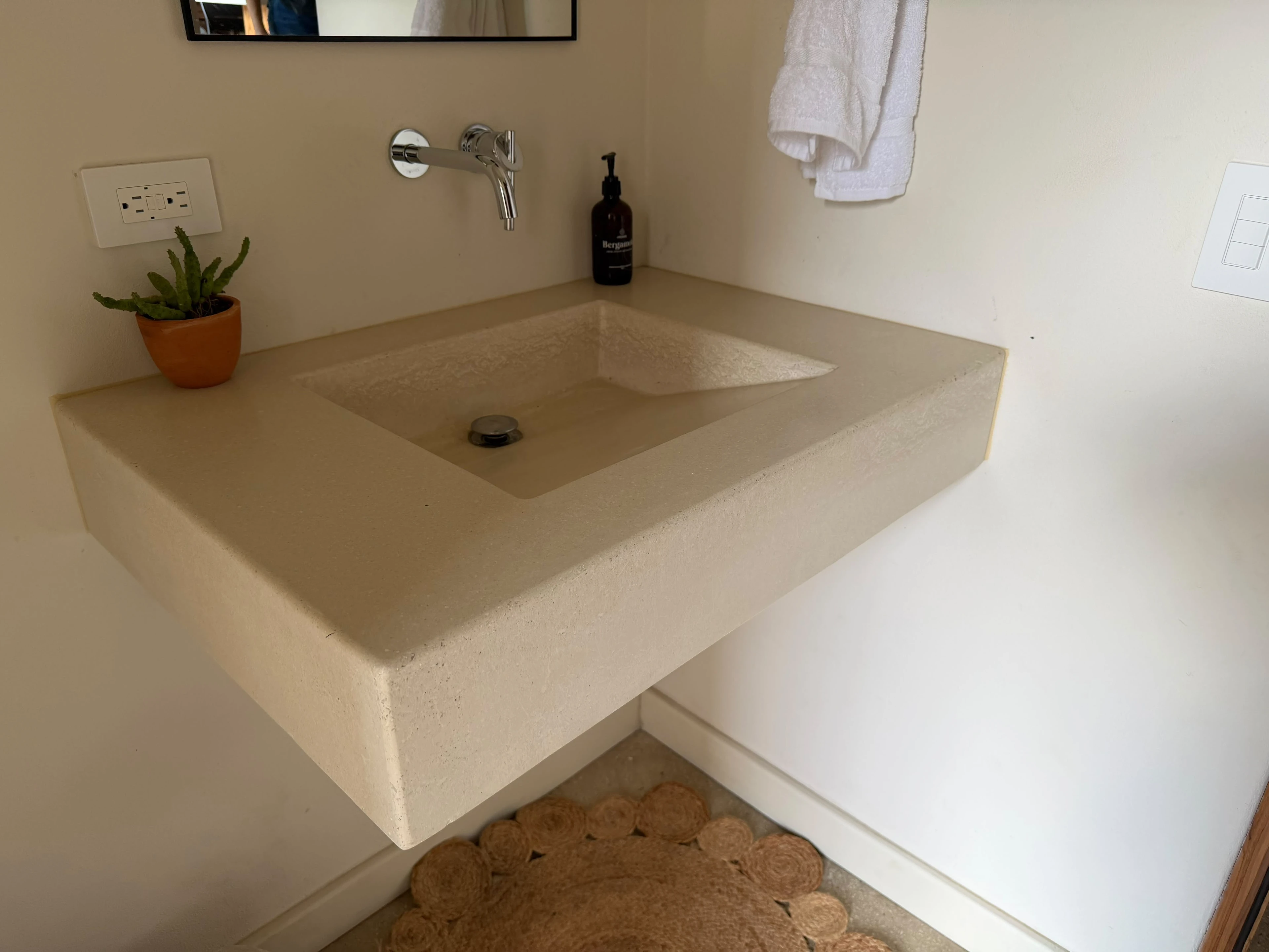 Lavatorio integrado flotante de concreto color crema con terminado granulado y poza inclinada, grifería de pared cromada