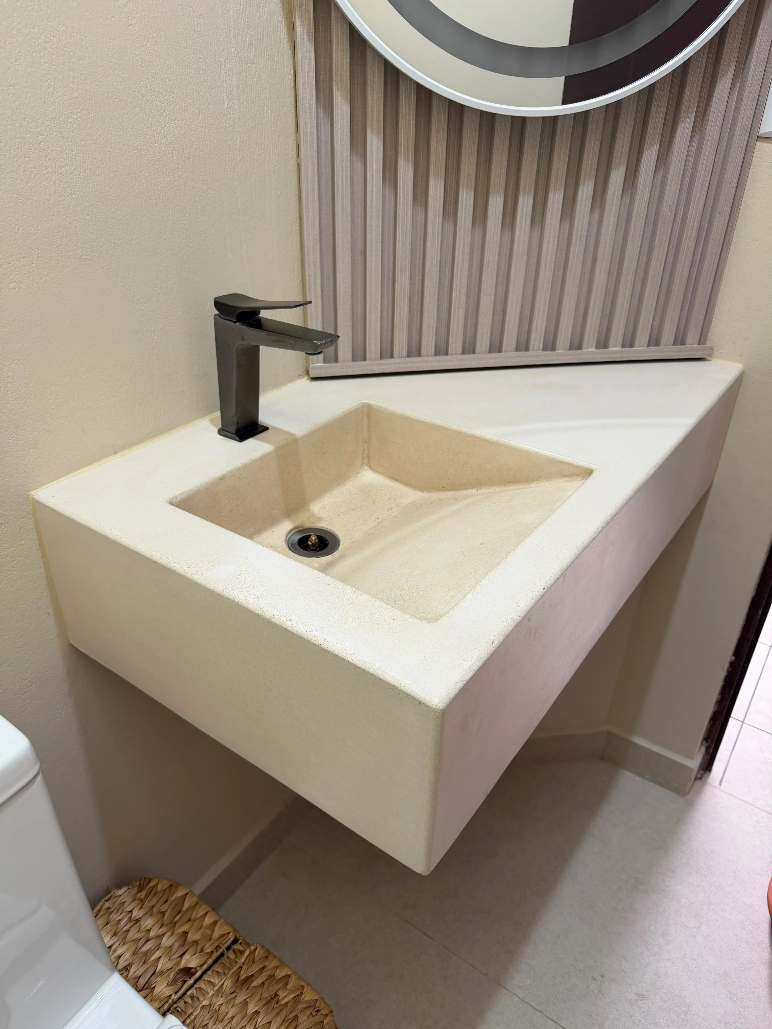 Lavatorio integrado de concreto crema con poza inclinada, grifería negra y desagüe cromado, en baño con espejo decorativo