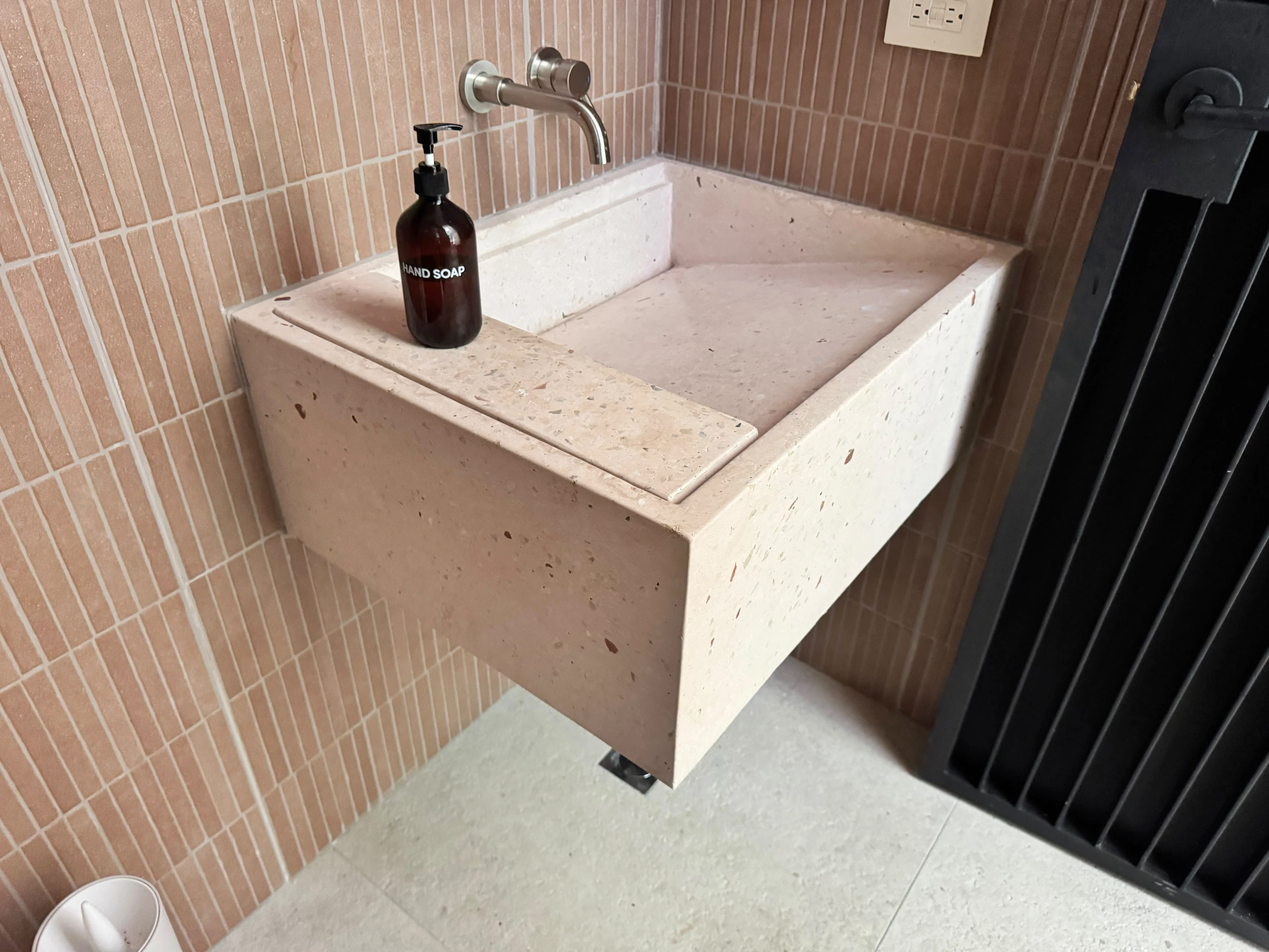 Lavatorio integrado de concreto rosado con poza rectangular inclinada y grifería cromada, sobre pared de azulejos alargados