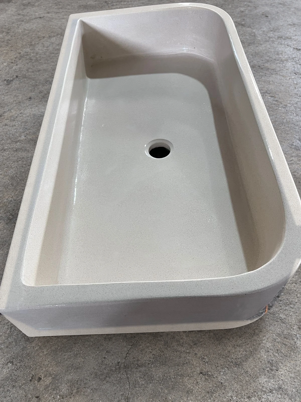 Pieza de lavatorio de concreto blanco con poza alargada de esquinas redondeadas y desagüe, apoyada sobre piso gris