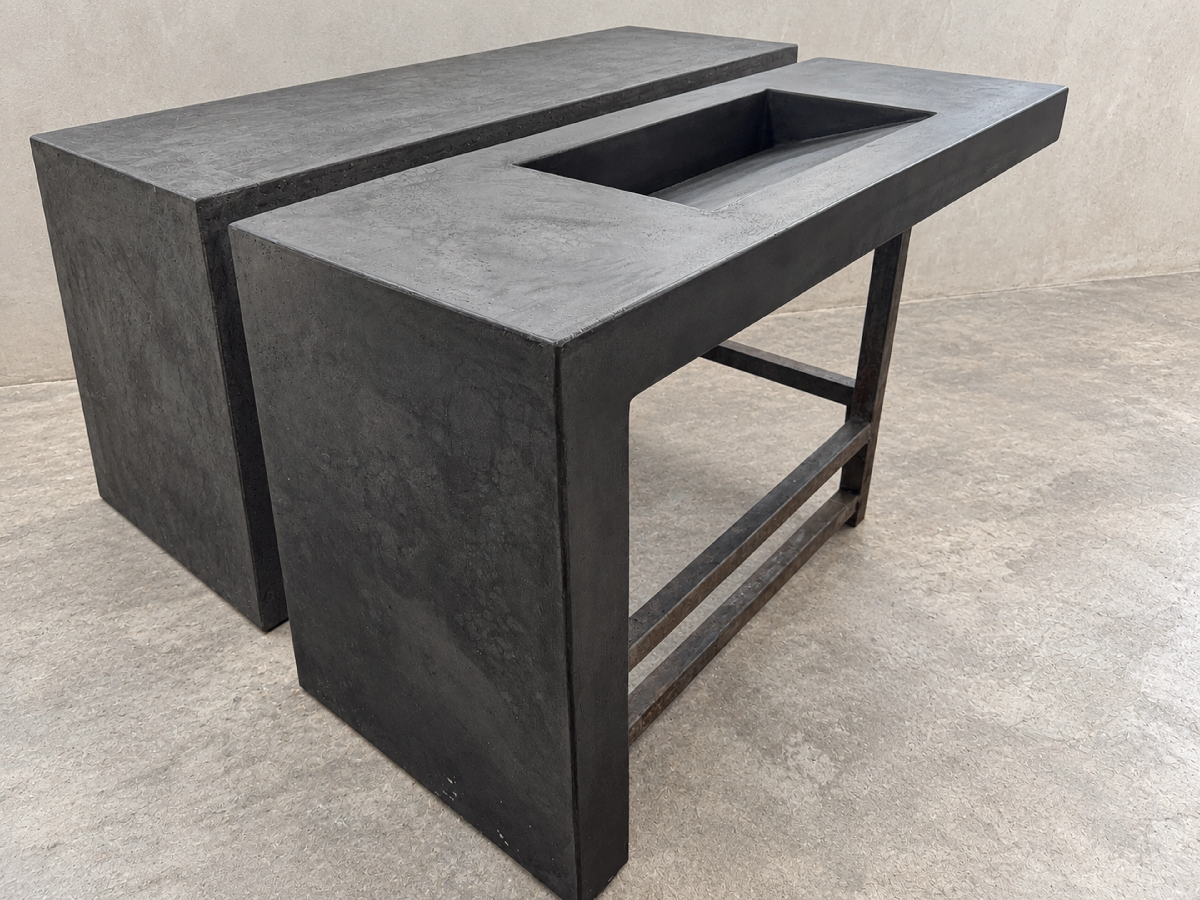 Mueble lavatorio de concreto gris oscuro con poza rectangular integrada y patas metálicas, en espacio de exhibición con piso gris
