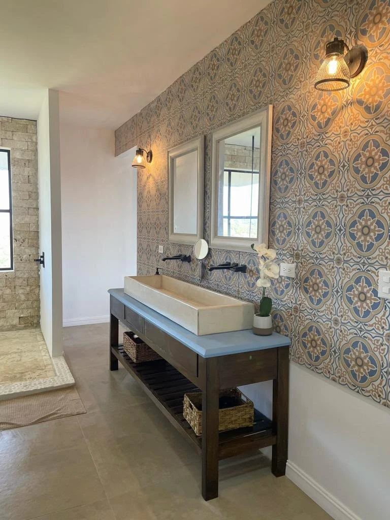 Lavatorio integrado de concreto claro con canal alargado sobre mesa de madera oscura, en baño con pared de azulejos decorados