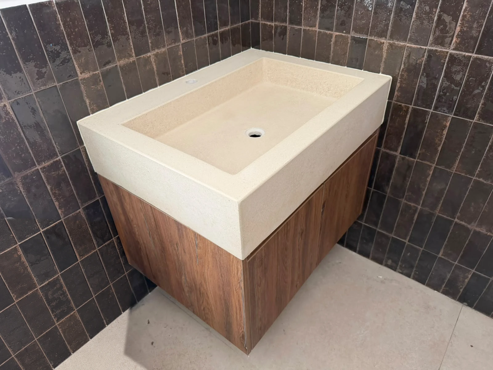 Lavatorio integrado de concreto crema con poza cuadrada, sobre mueble de madera flotante y pared de azulejos color café
