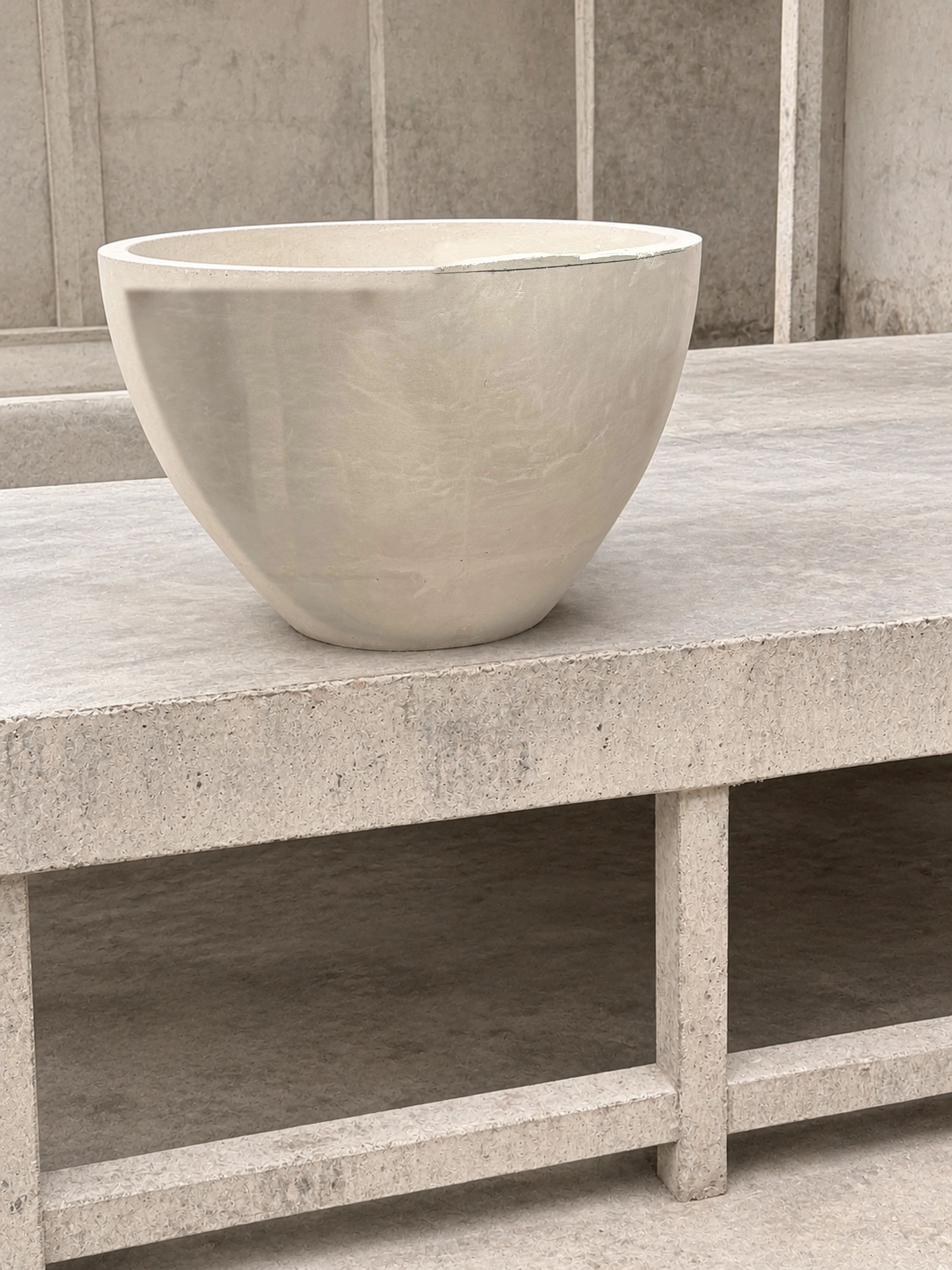 Lavatorio de sobreponer de concreto gris claro con forma de tazón alto, sobre encimera de concreto con estructura de soportes