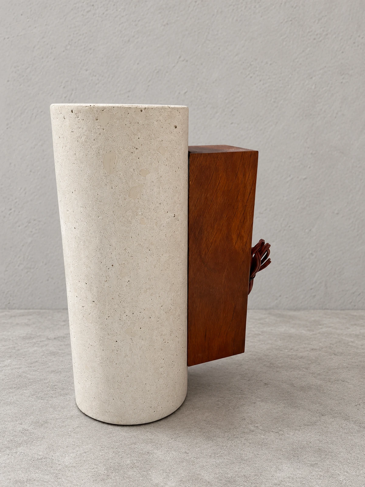 Lavatorio de pedestal cilíndrico de concreto blanco con agregados visibles y un bloque de madera oscura, sobre fondo gris