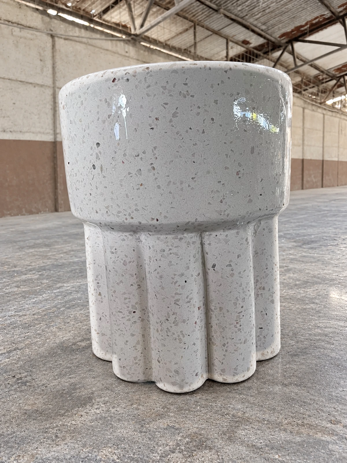Lavatorio de pedestal de terrazo blanco con agregados oscuros, acabado brillante y base ondulada, en una nave de piso pulido