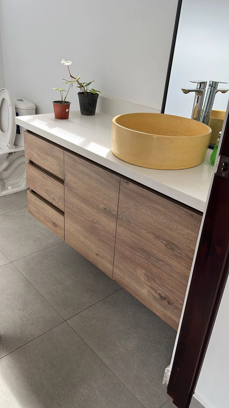 Lavatorio de sobreponer redondo de concreto amarillo sobre encimera blanca con mueble de madera flotante y grifería cromada