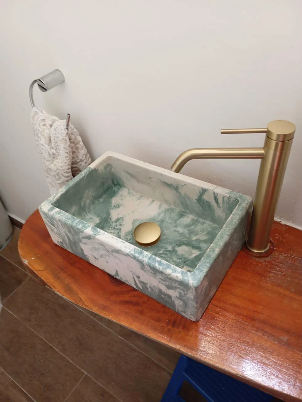 Lavatorio de sobreponer rectangular de concreto marmoleado verde y blanco sobre encimera de madera, con grifería dorada
