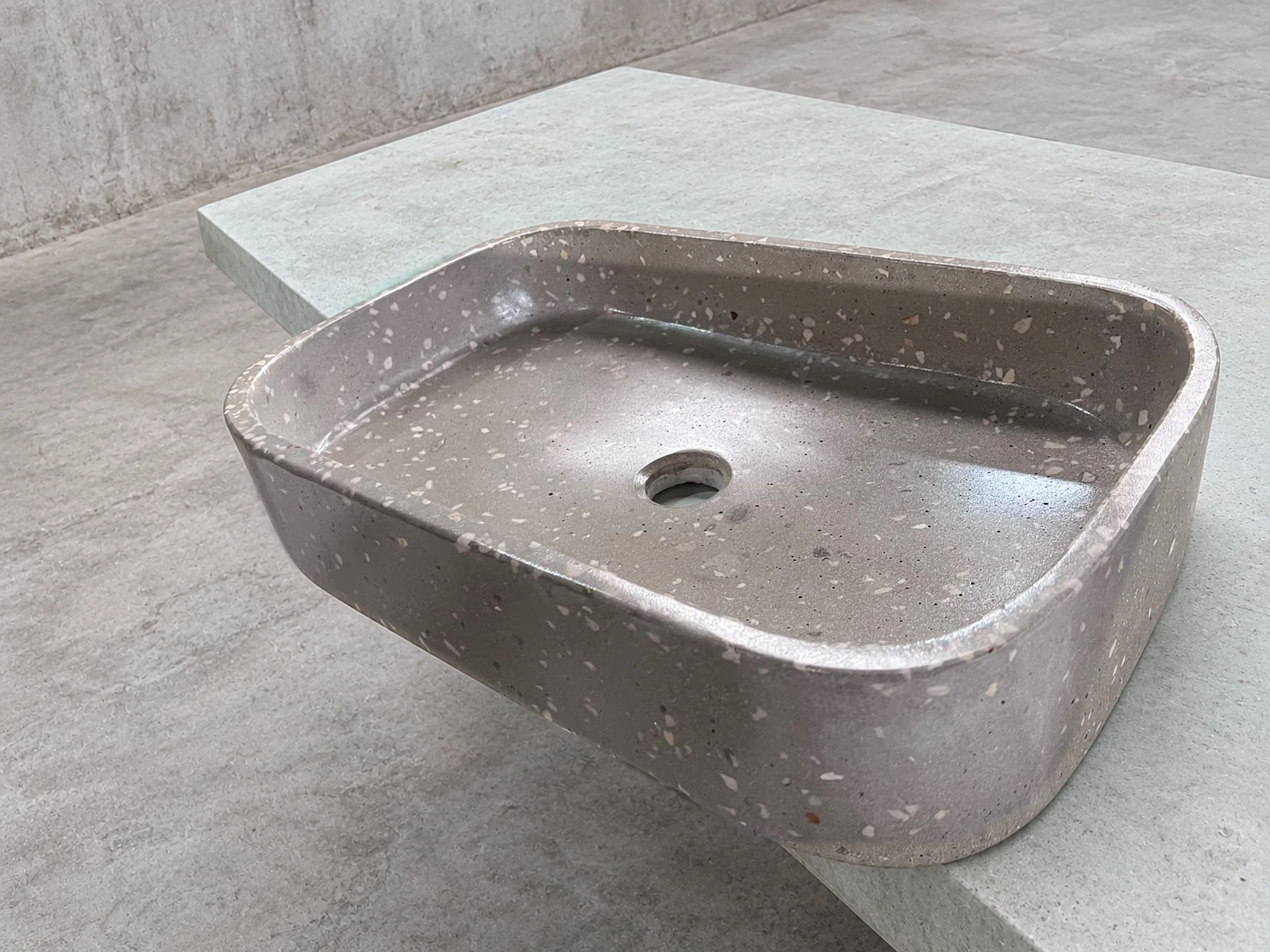 Lavatorio de sobreponer rectangular de concreto gris con agregados claros y esquinas redondeadas, sobre encimera verde pálido