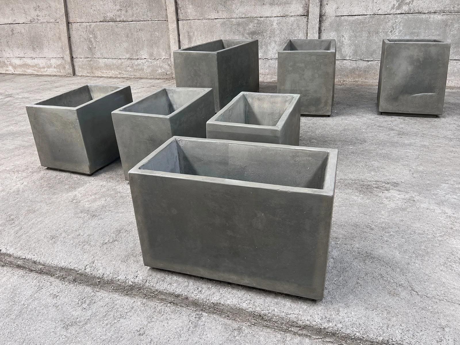 Conjunto de maceteros rectangulares y cuadrados de concreto gris de varios tamaños, sobre piso de cemento
