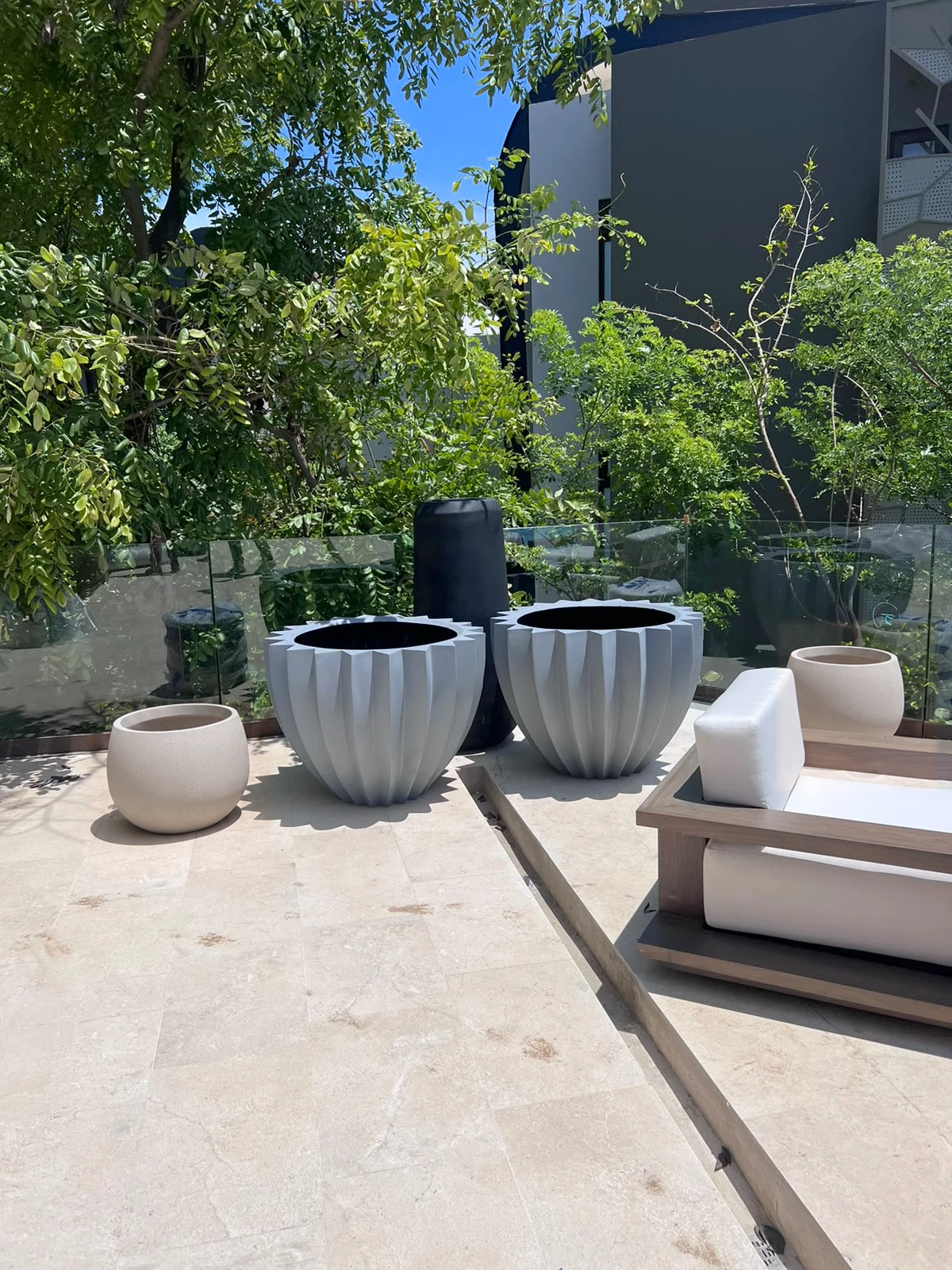 Maceteros acampanados de concreto gris claro con paredes acanaladas y otros más pequeños, sobre terraza con muebles