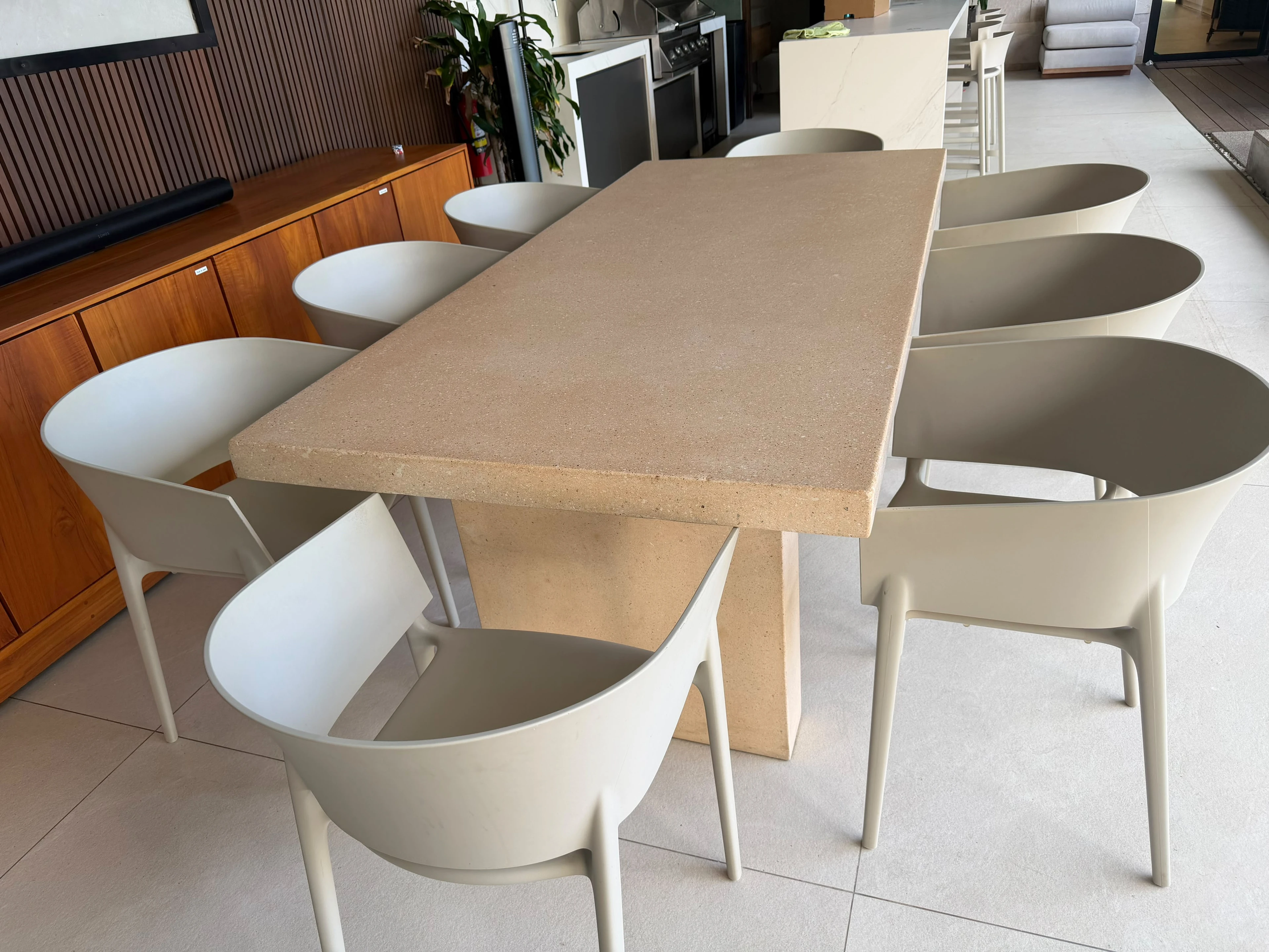 Mesa de comedor rectangular de concreto color arena con pedestal central y sillas claras, en comedor con mueble de madera