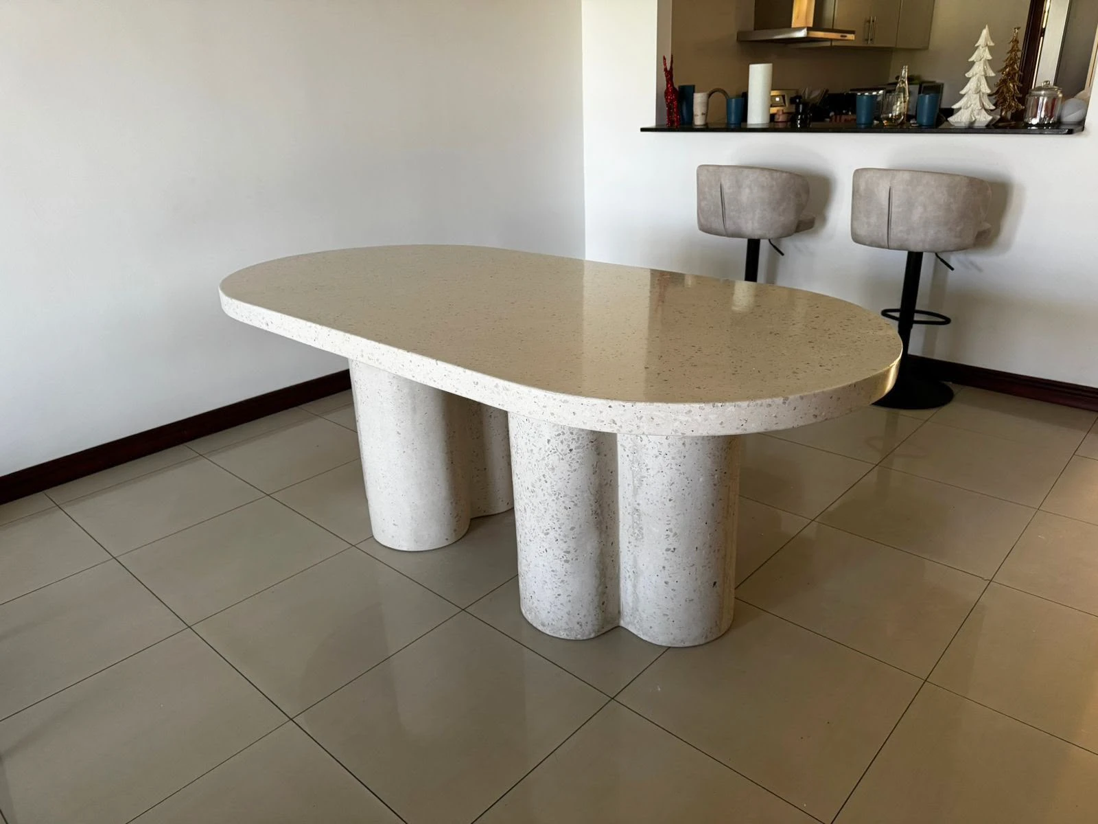Mesa de comedor ovalada de terrazo color arena con patas en forma de trébol, en comedor con piso de porcelanato