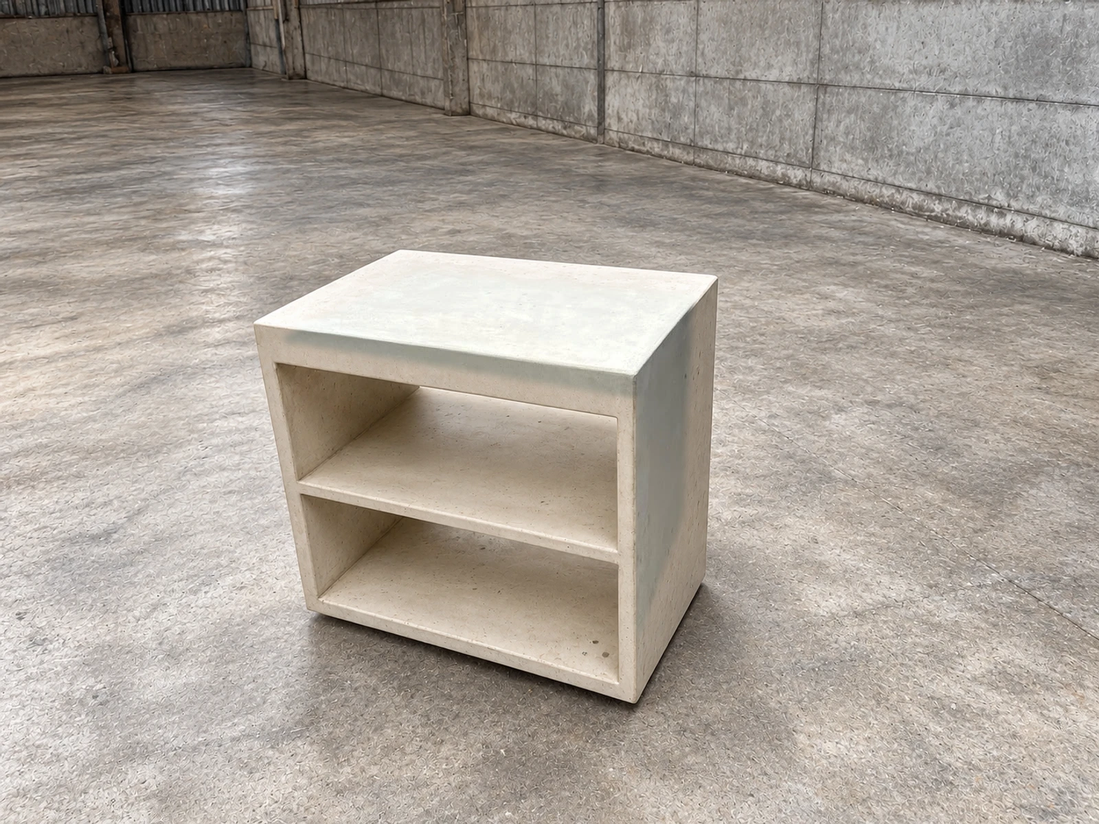 Mueble auxiliar cúbico de concreto color crema con dos repisas abiertas, sobre piso de cemento pulido