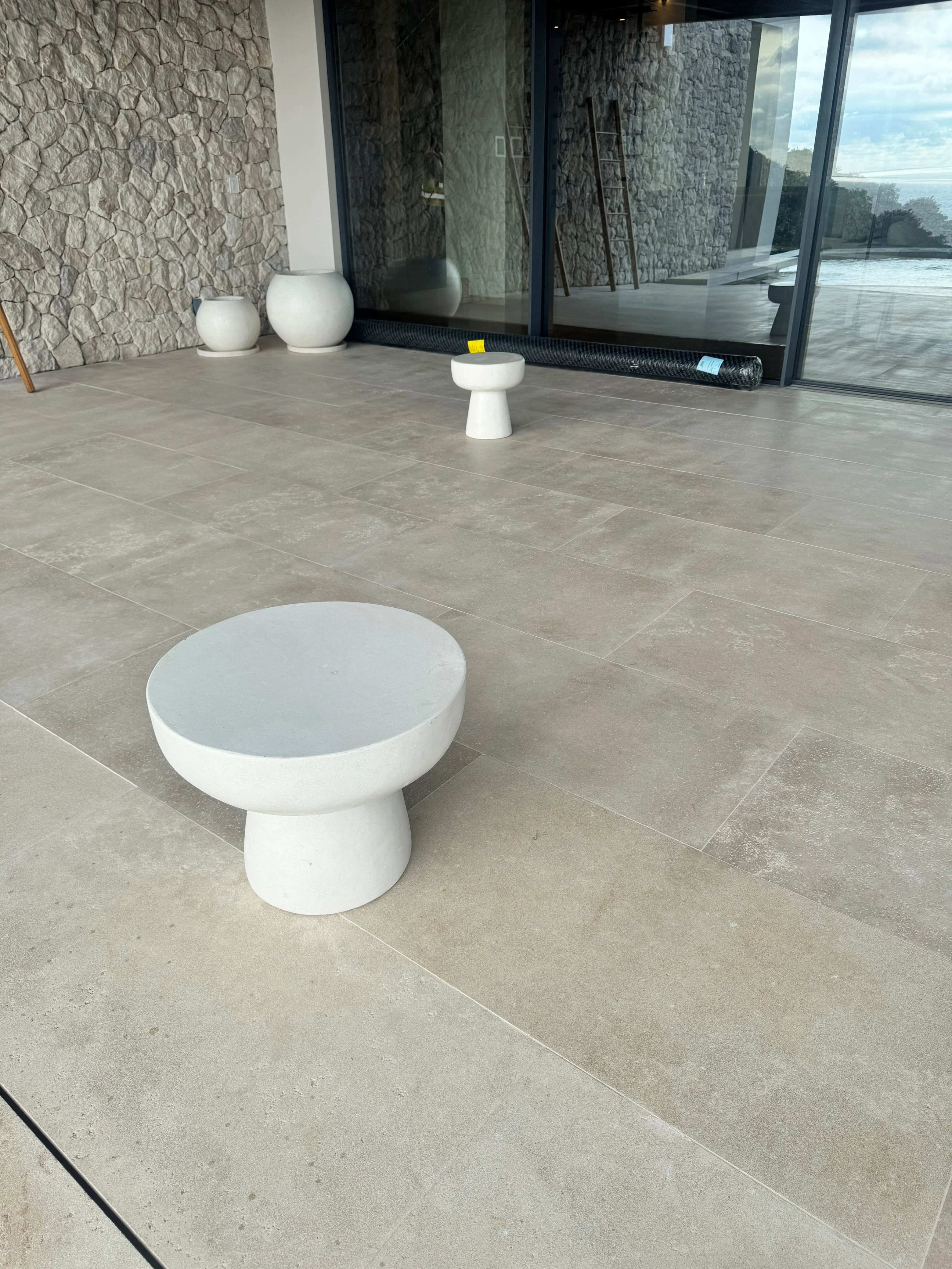 Mesa auxiliar baja de concreto blanco con tapa redonda y pie en forma de hongo, sobre piso claro en terraza