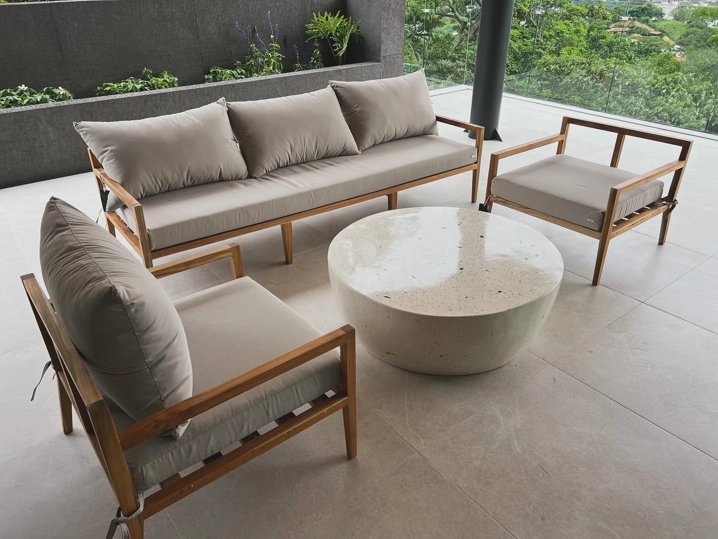 Mesa de centro redonda de concreto blanco con forma de tazón invertido, frente a sofá y sillones de madera en terraza