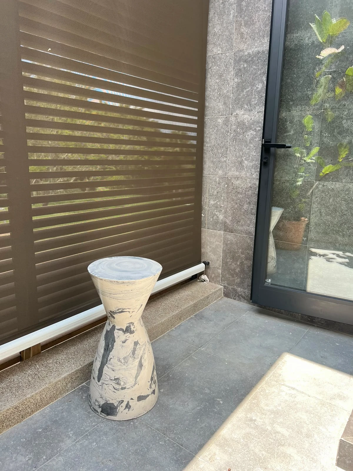 Mesa auxiliar en forma de reloj de arena con vetas marmoleadas en blanco, gris y beige, junto a una puerta de vidrio