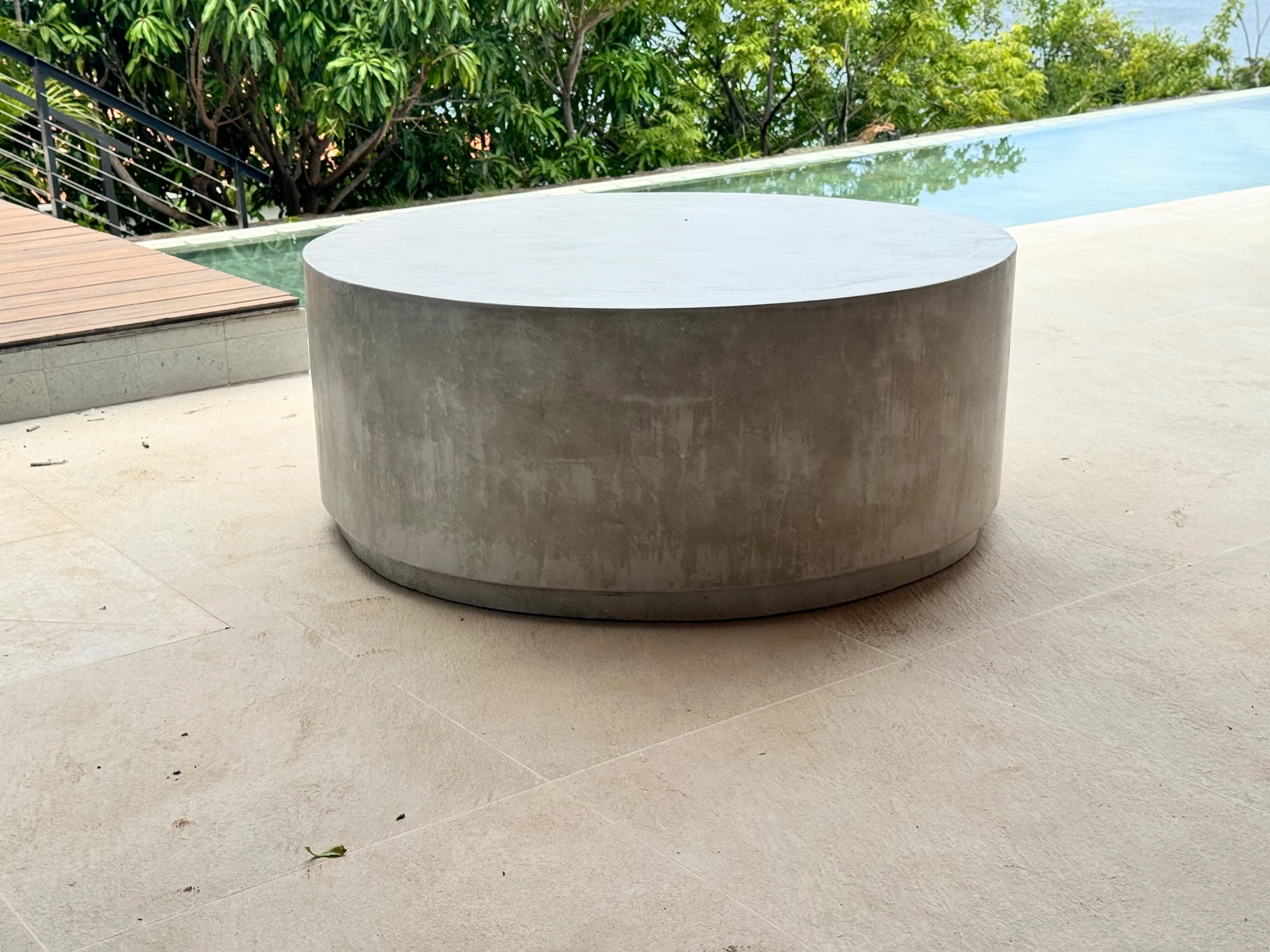 Mesa de centro redonda y baja de concreto gris liso, con borde recto, sobre terraza junto a una piscina