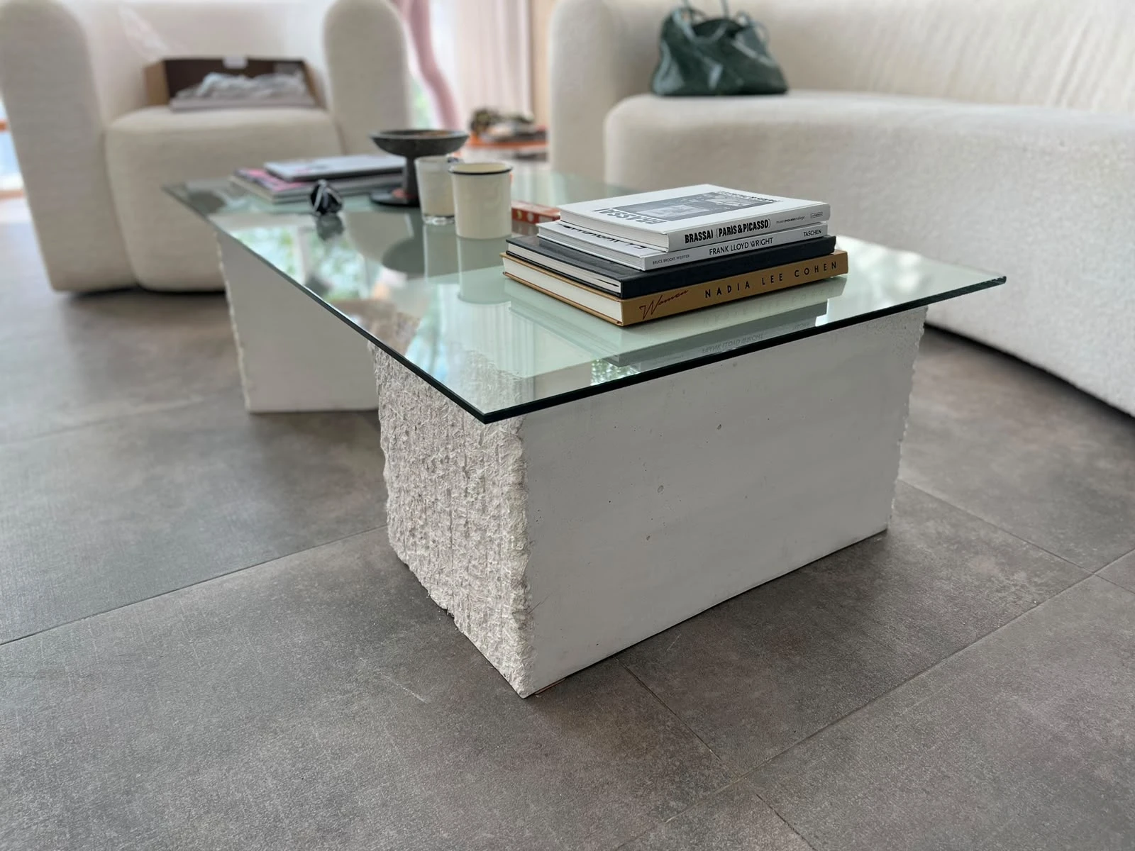 Mesa de centro con tapa de vidrio sobre base de concreto blanco de textura rústica, en sala con sofás blancos