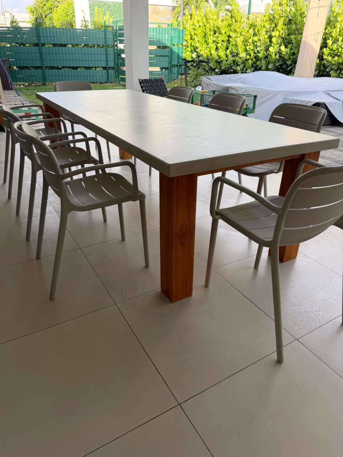 Mesa de comedor rectangular con tapa de concreto gris y patas de madera, con sillas grises, en terraza techada
