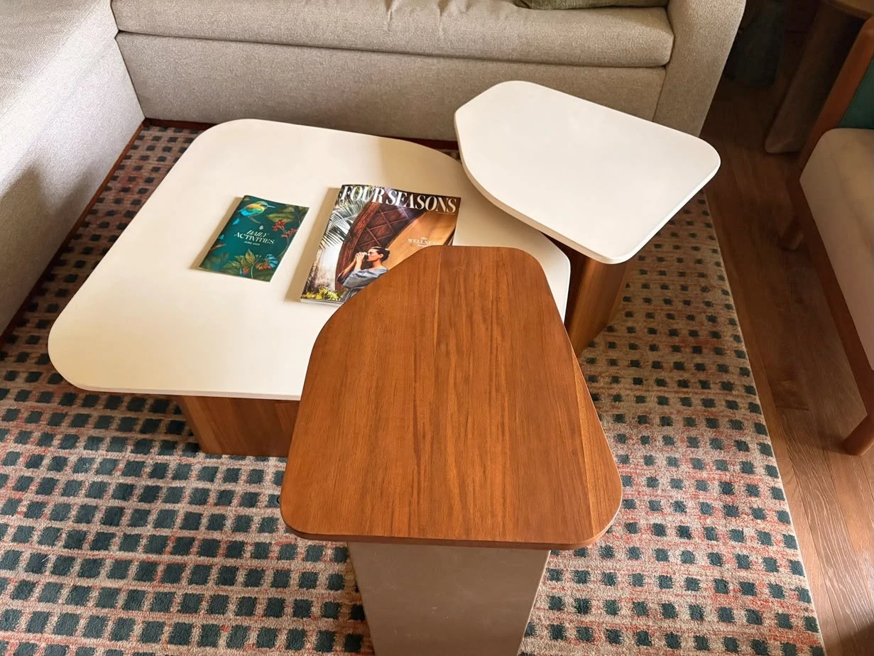 Conjunto de mesas de centro de formas orgánicas con tapas crema y de madera, sobre alfombra de cuadros en sala con sofá