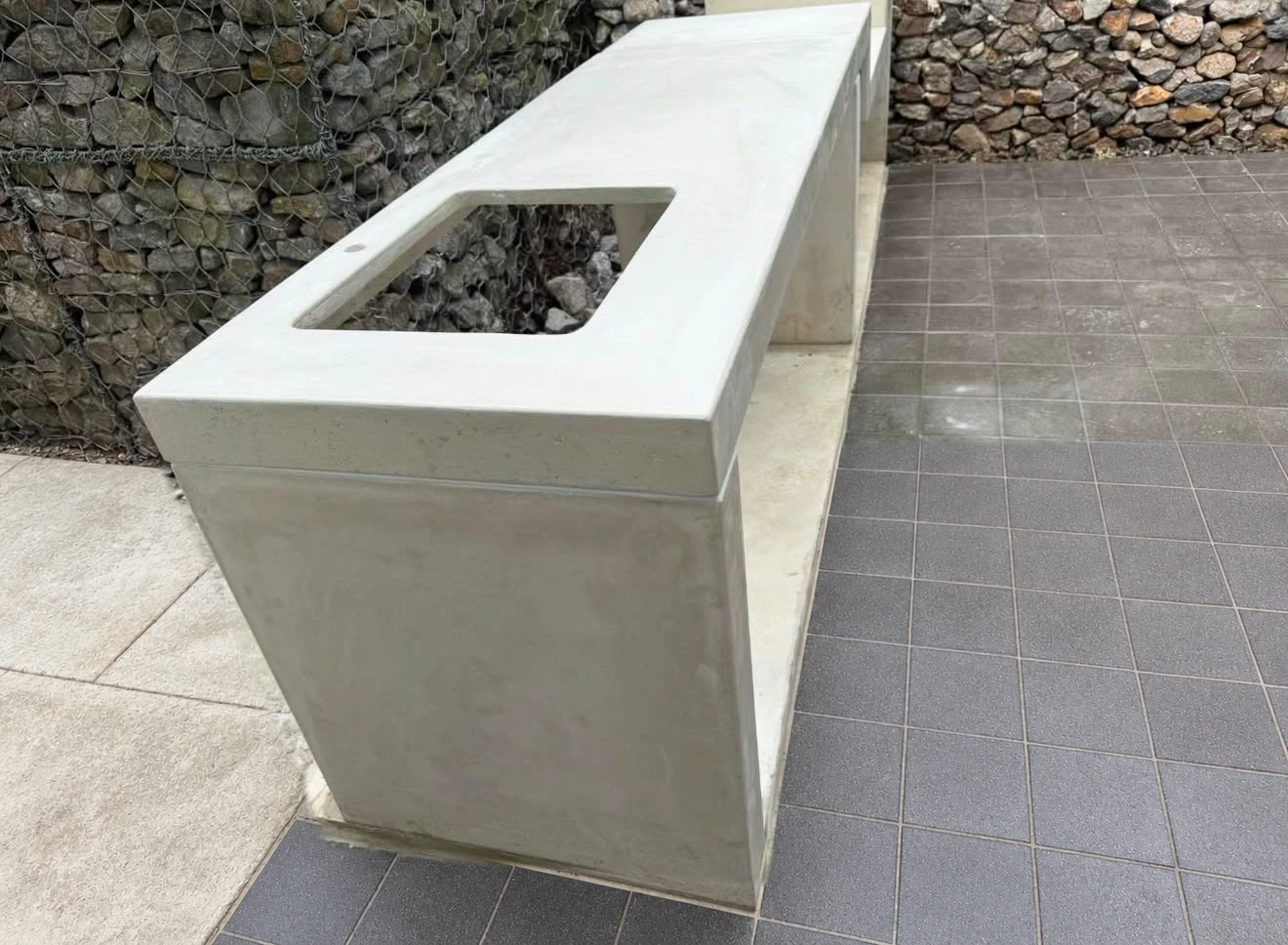 Pila de concreto blanco con poza rectangular integrada a un mueble con espacio abierto, junto a muro de piedra en patio exterior