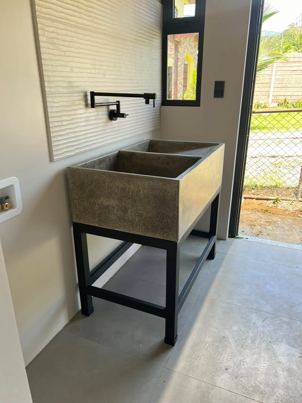 Pila de concreto gris verdoso con poza rectangular profunda, sobre estructura metálica negra, con grifería negra articulada en pared