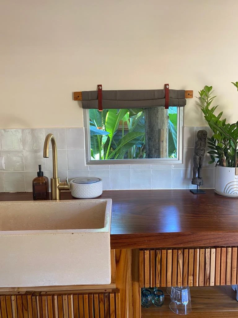 Pila de concreto color crema con frente liso tipo delantal, junto a grifería dorada y encimera de madera en cocina rústica