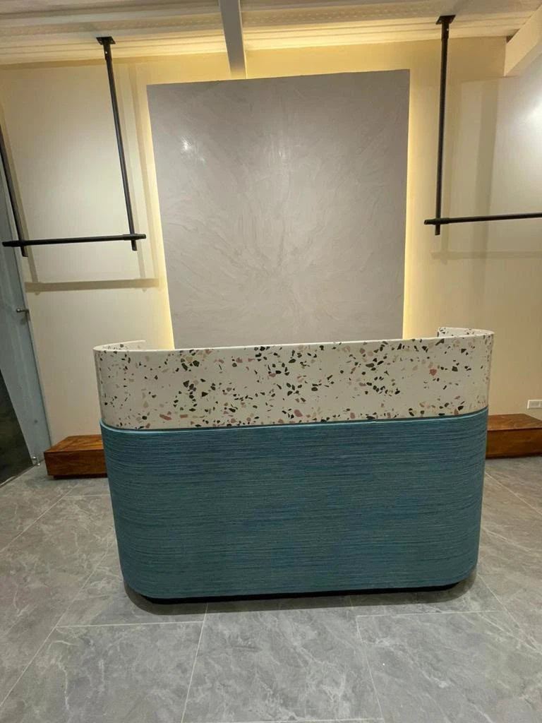 Mostrador curvo con sobre de terrazo claro con agregados oscuros y frente de concreto azul acanalado, en recepción con piso gris