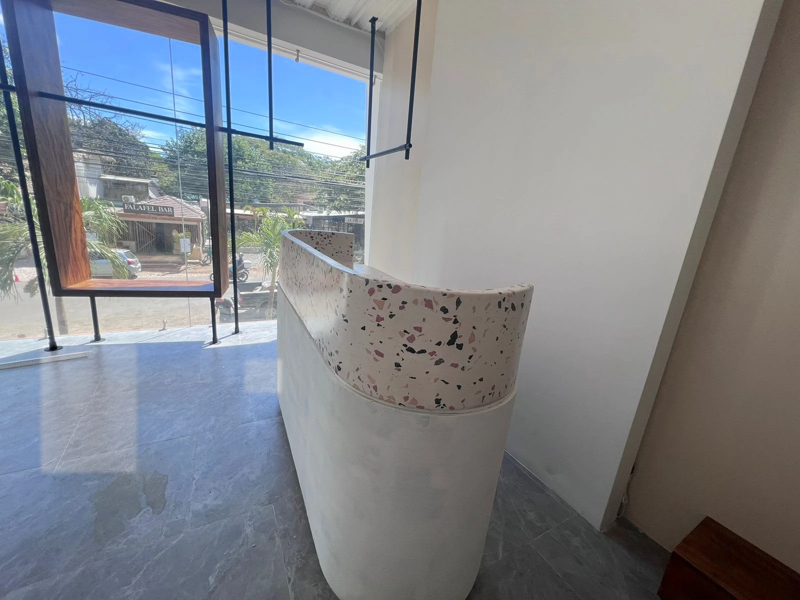 Mostrador curvo de recepción con sobre de terrazo con agregados de colores y base blanca, junto a un ventanal, vista lateral