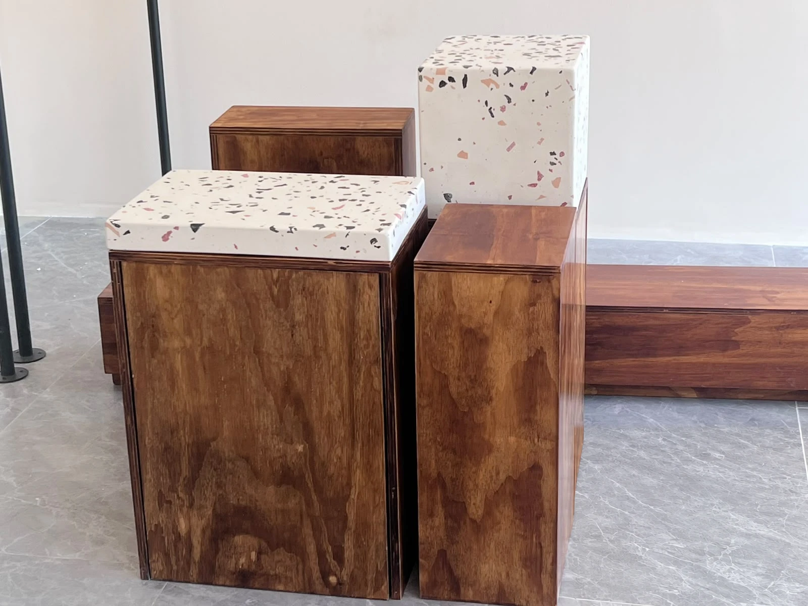 Sobres de terrazo blanco con agregados rosados y grises apoyados sobre pedestales de madera, en sala de exhibición
