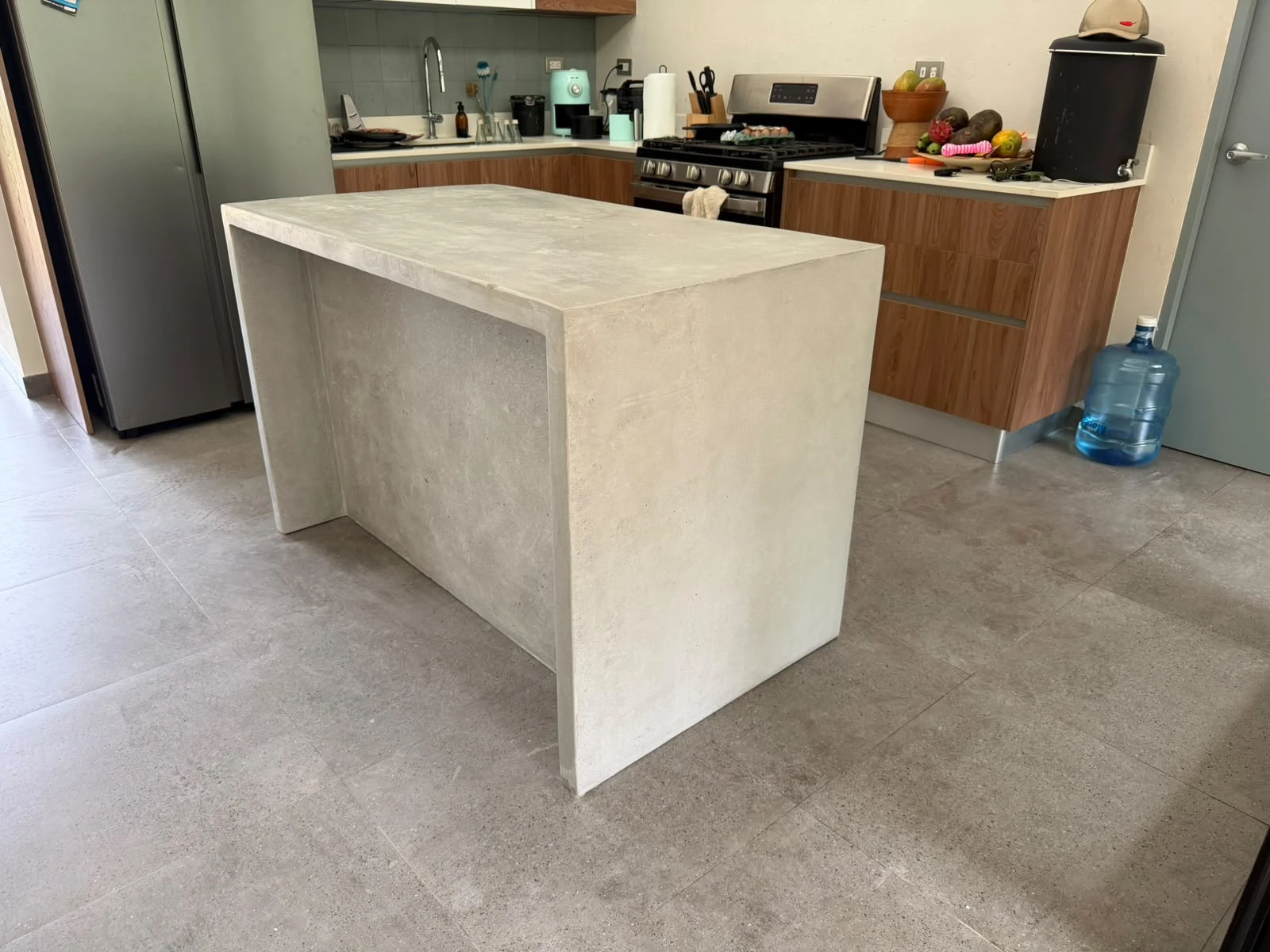 Isla de cocina de concreto gris claro con sobre y laterales continuos en cascada, en una cocina con muebles de madera