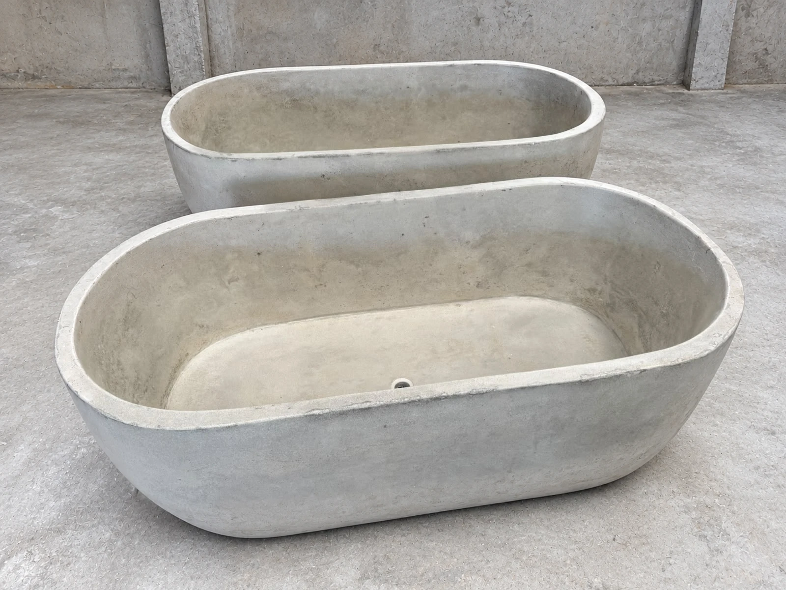Dos tinas ovaladas de concreto gris claro de distinto tamaño, con interior liso y desagüe, sobre piso de cemento en bodega