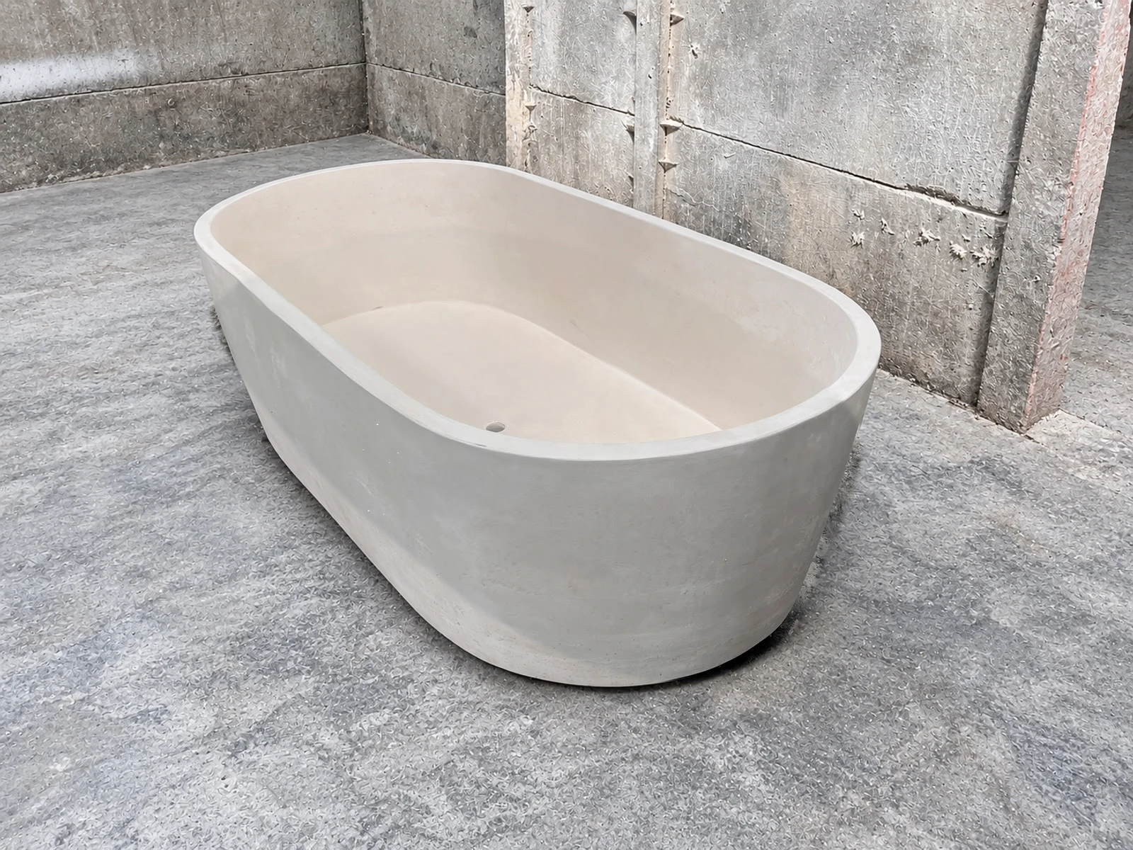 Tina ovalada de concreto de dos tonos, con interior crema y exterior gris claro, sobre piso de cemento en bodega