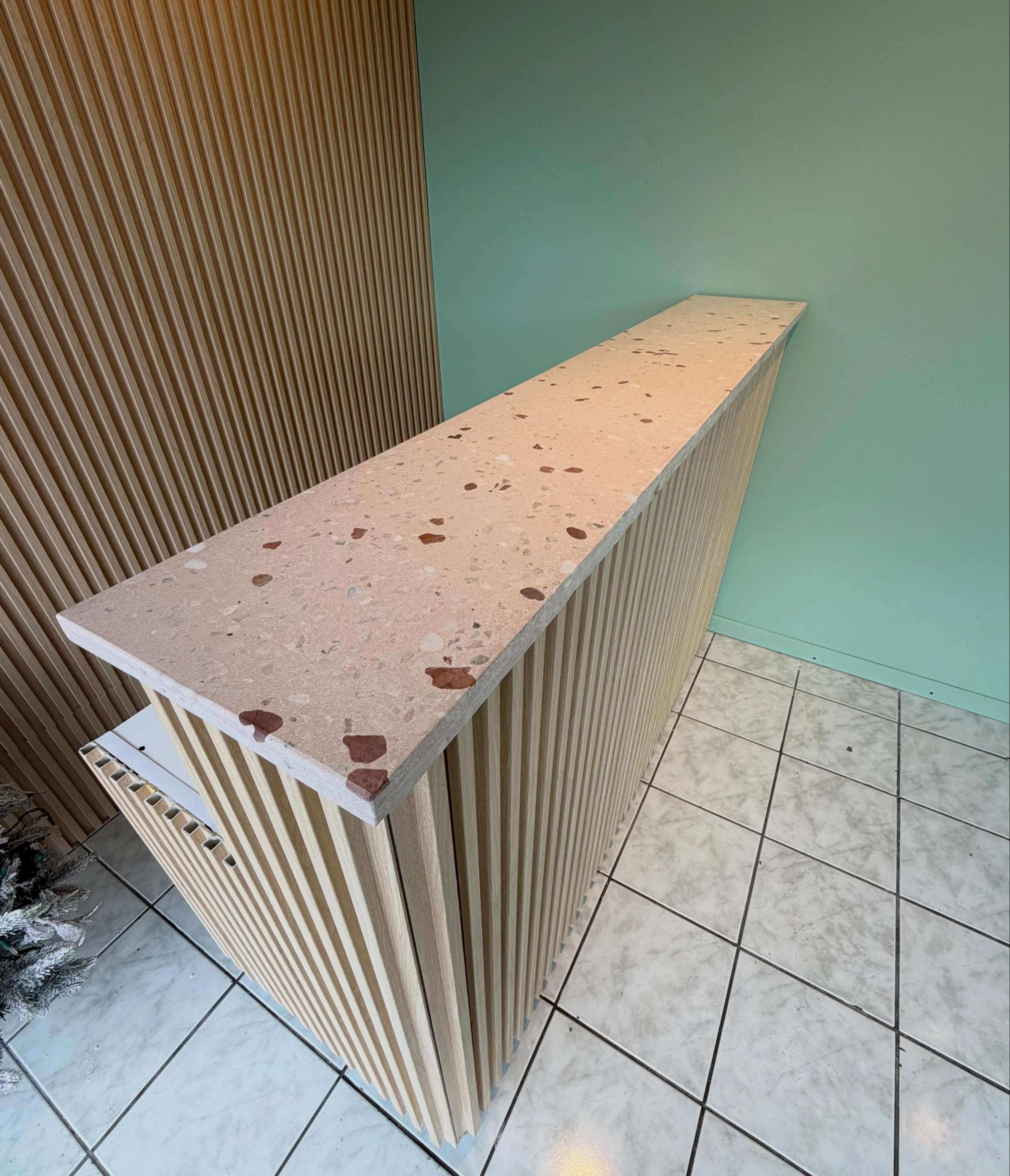 Barra angosta de terrazo rosado con agregado rojo y blanco, sobre base de listones de madera clara