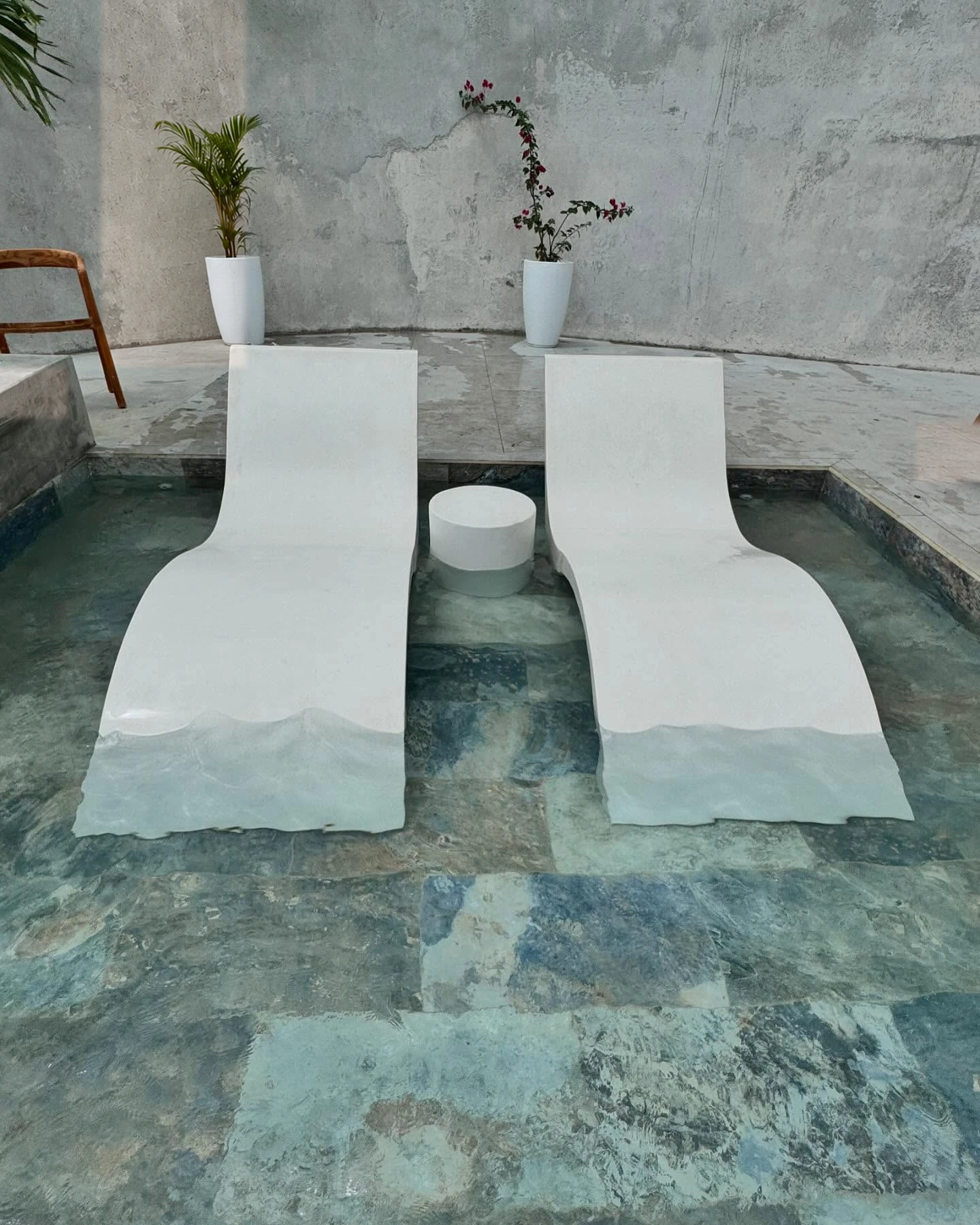 Dos camastros curvos de concreto blanco dentro de una piscina poco profunda, con vista al mar y vegetación. Vista adicional 2.