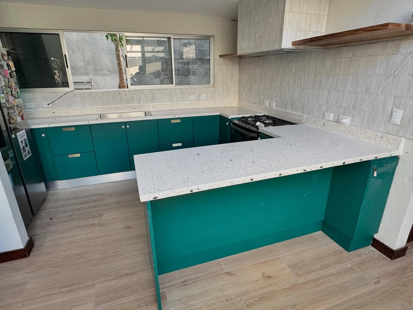 Cocina en L con sobre continuo de terrazo blanco y mueble bajo turquesa