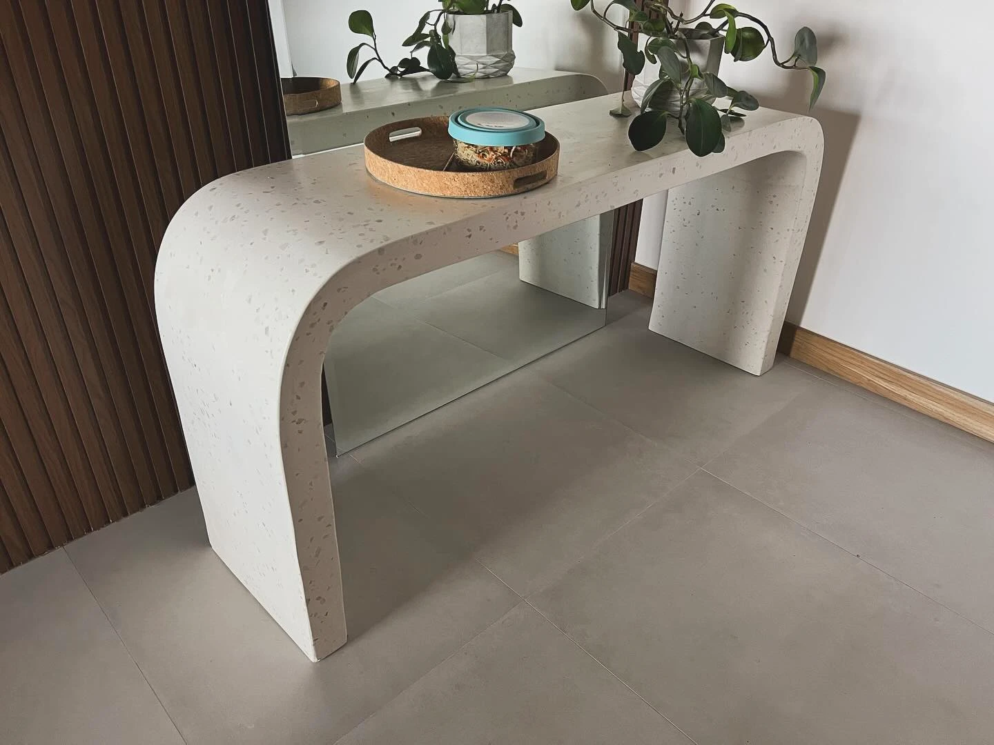Consola de concreto claro doblada en curva continua desde el sobre hasta el piso, contra una pared blanca