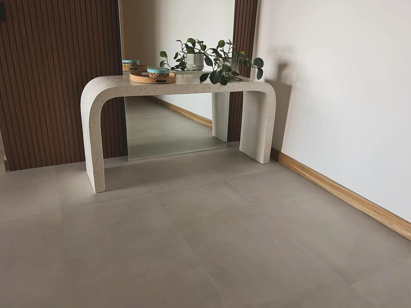 Consola de concreto claro doblada en curva continua desde el sobre hasta el piso, contra una pared blanca. Vista adicional 1.