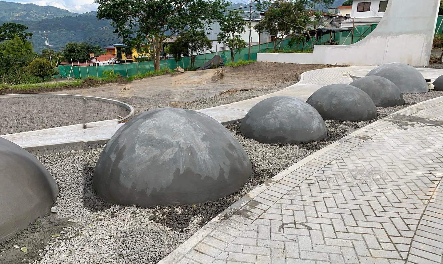 Esferas de concreto gris ya instaladas sobre grava a lo largo de un sendero de parque, con montañas al fondo