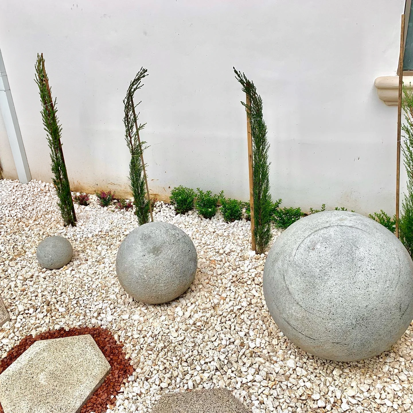 Dos esferas de concreto gris sobre grava blanca, contra un muro blanco con plantas verticales