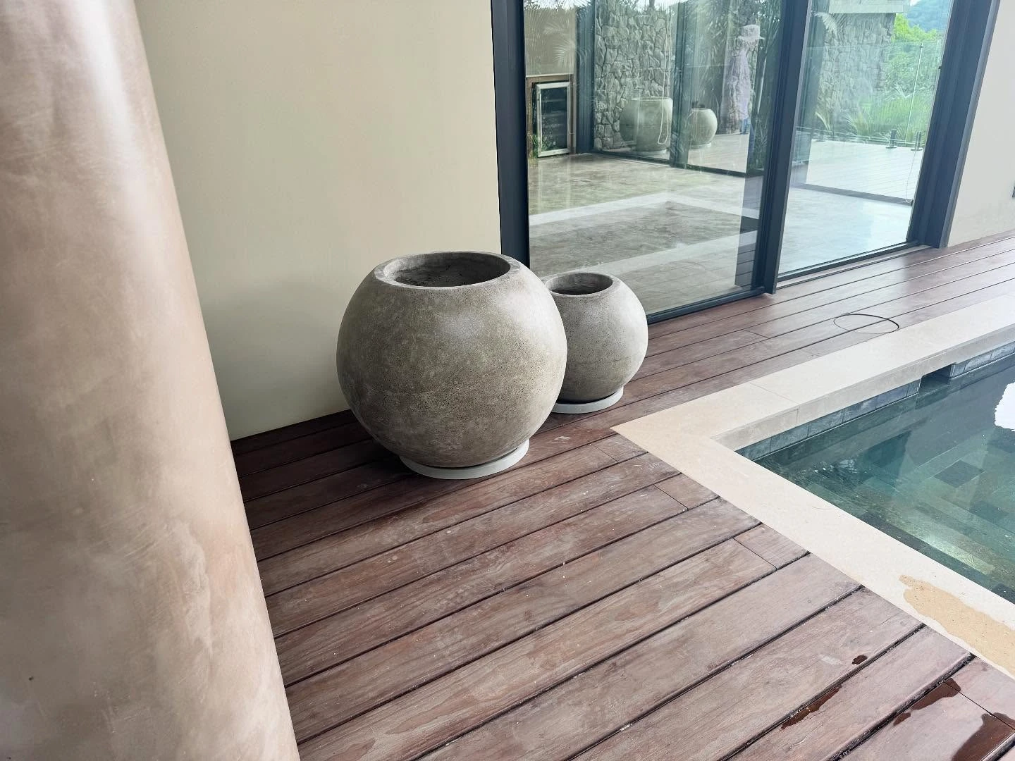 Dos maceteros esféricos de concreto claro sobre un deck de madera junto al borde de una piscina