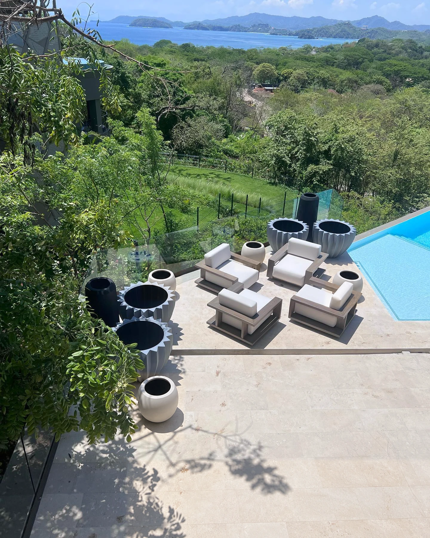 Maceteros negros de concreto distribuidos en una terraza con camastros y piscina, vistos desde arriba
