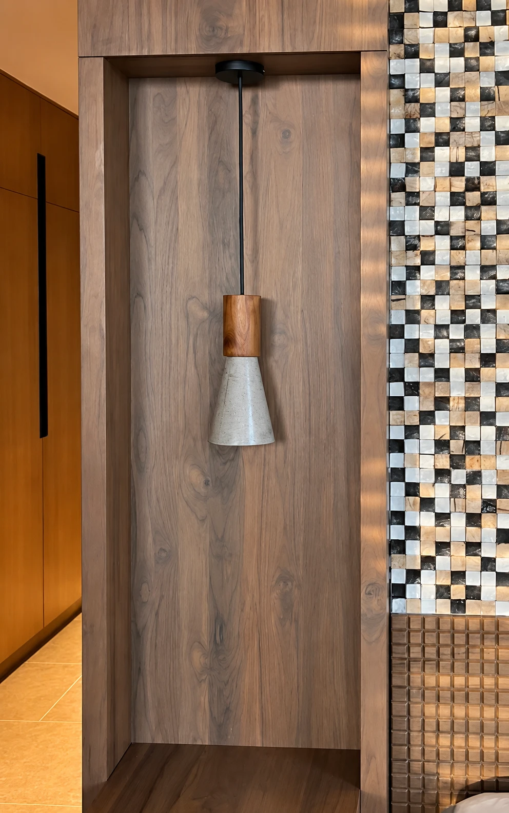 Lámpara colgante de pantalla cónica de concreto claro y cuello de madera, en un nicho de pared entablillada