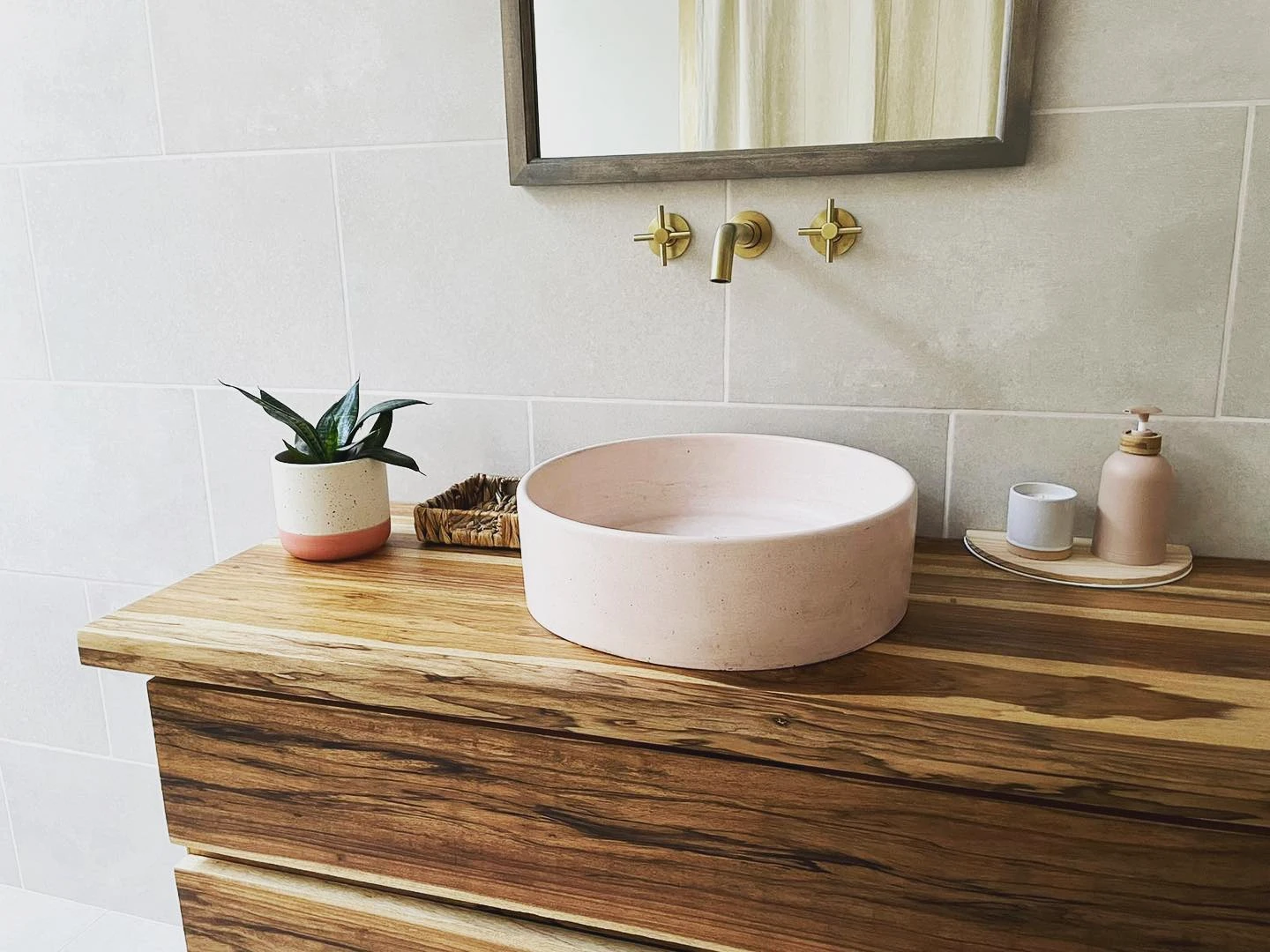 Lavatorio redondo de concreto rosa pálido sobre un sobre de madera veteada, con grifería de pared en bronce