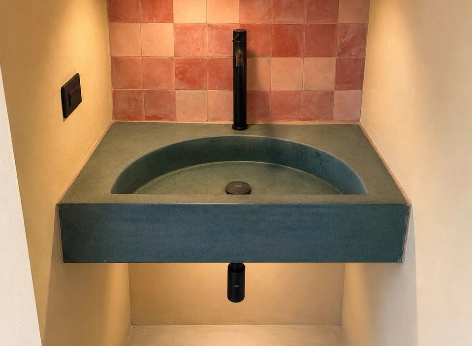 Lavatorio de concreto turquesa con poza integrada, contra una pared de azulejo terracota