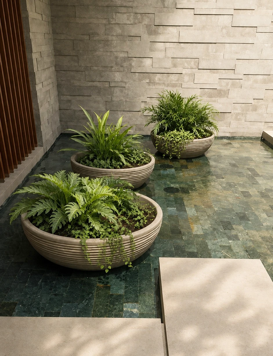 Tres maceteros bajos en forma de cuenco, con estriado horizontal, sobre un piso de mosaico verde en un patio interior